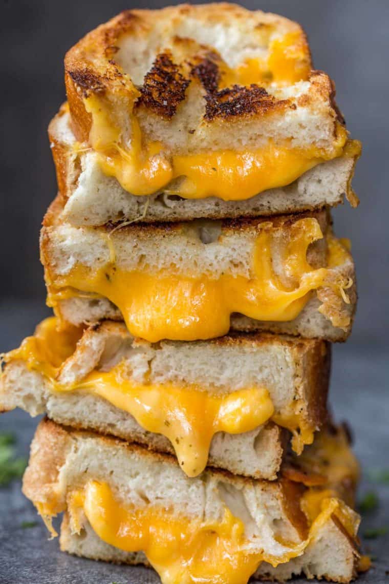 Grilled cheese sandwiches stacked on top top of each other with cheese oozing out.
