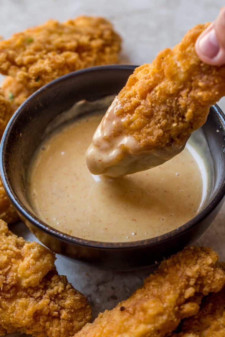 A bowl of creamy honey mustard sauce next to chicken tenders. 