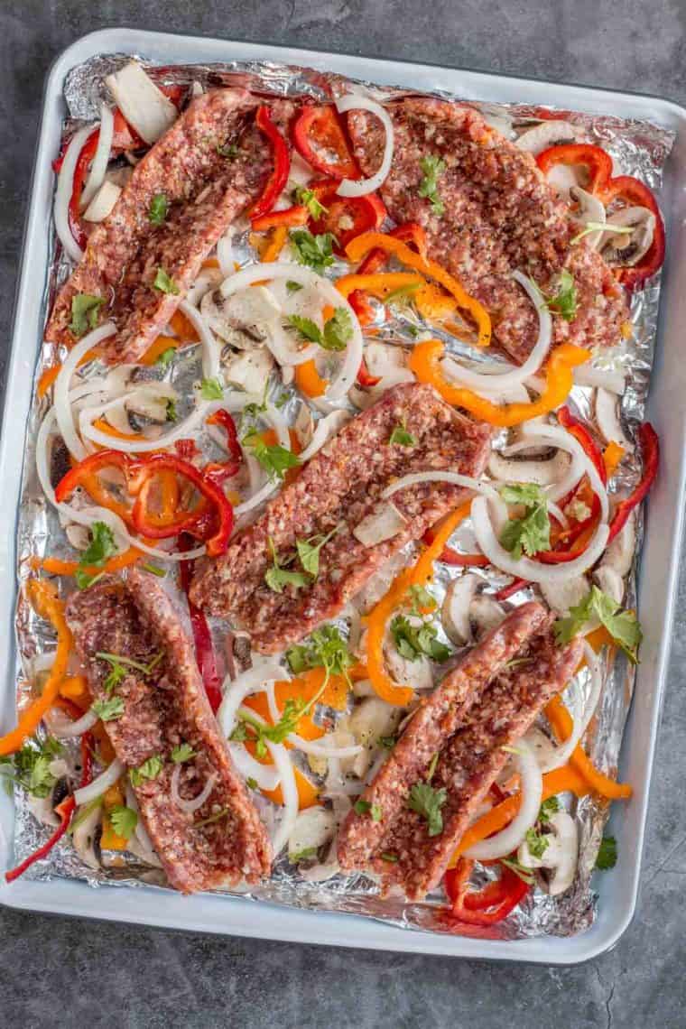 Butterflied sausages with sliced vegetables on a platter for grilling.