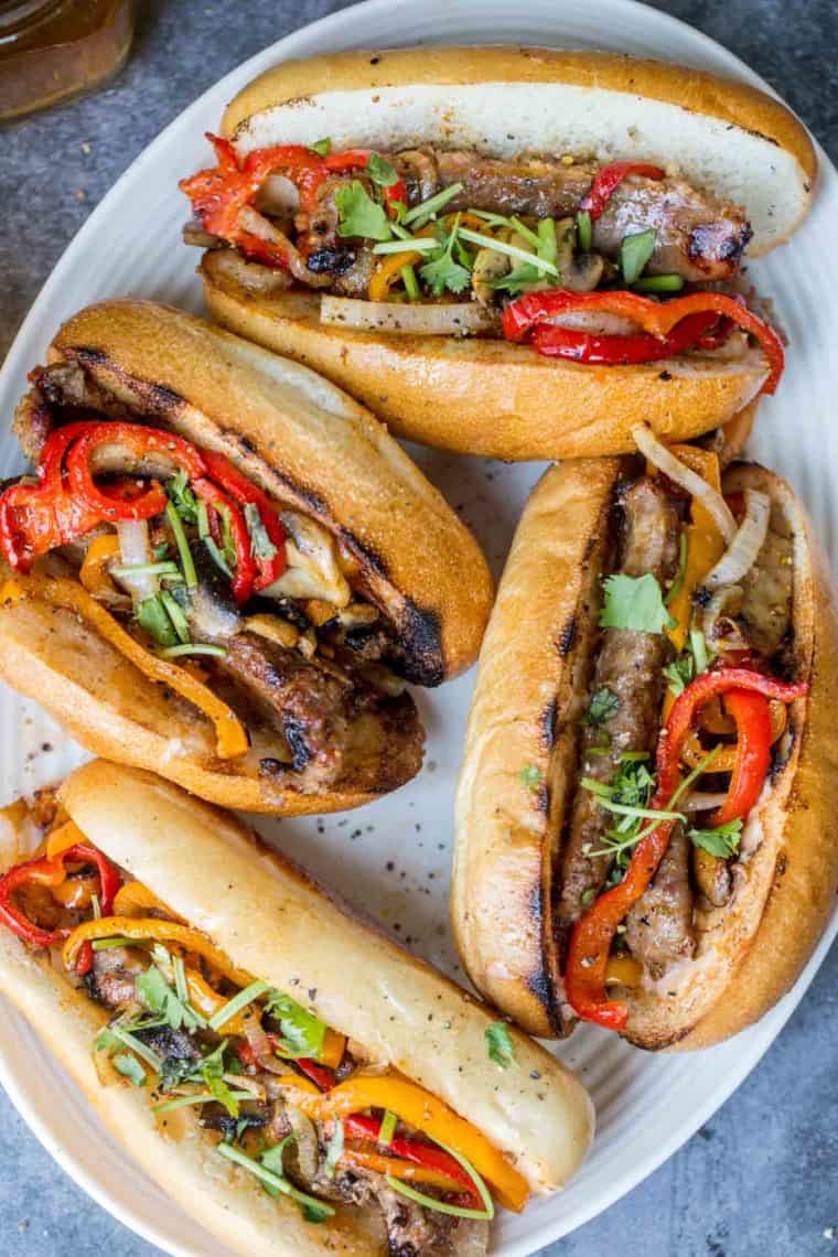 Grilled italian mild sausages in a hoagie topped with grilled vegetables on a plate. 