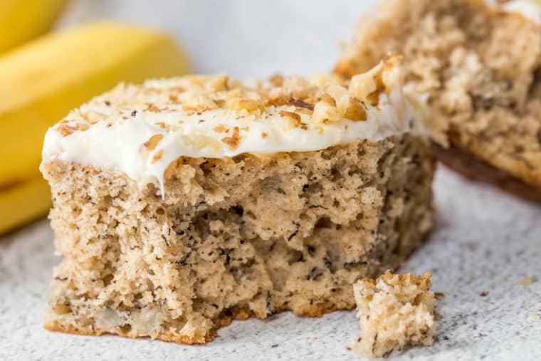A slice of moist banana coffee cake topped with cream cheese frosting and chopped walnuts. 