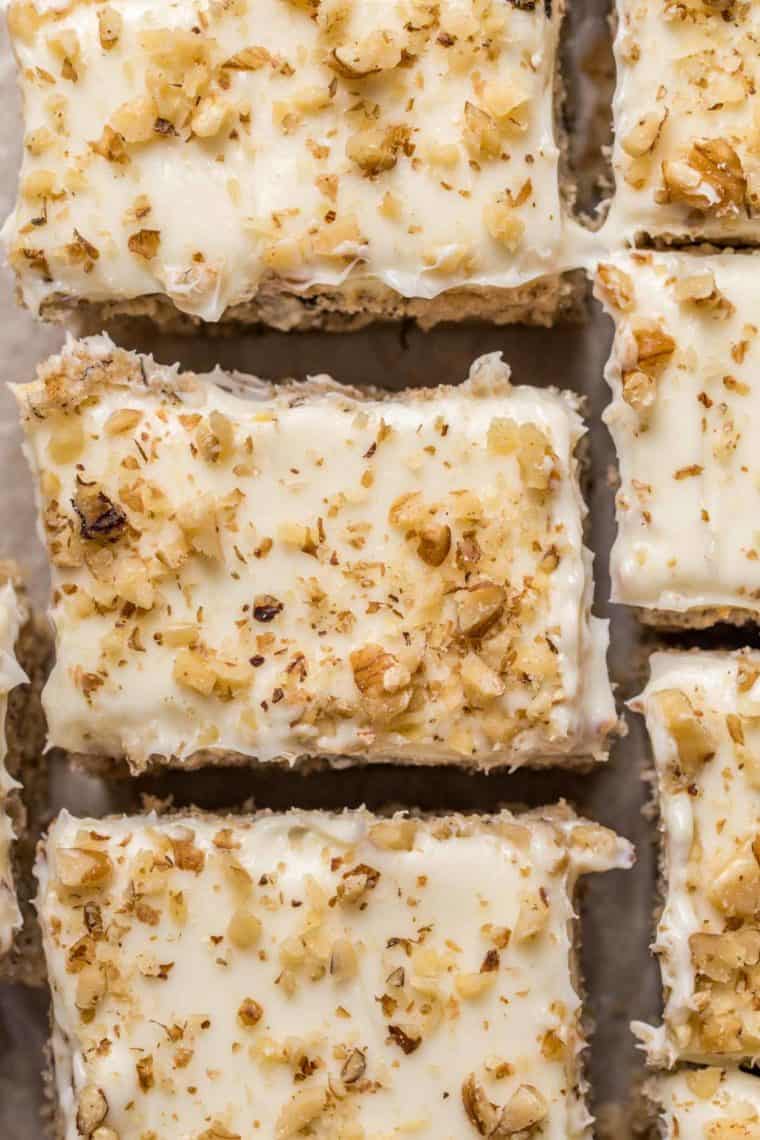 Slices of banana coffee cake topped with cream cheese frosting and walnuts laid out next to each other. 
