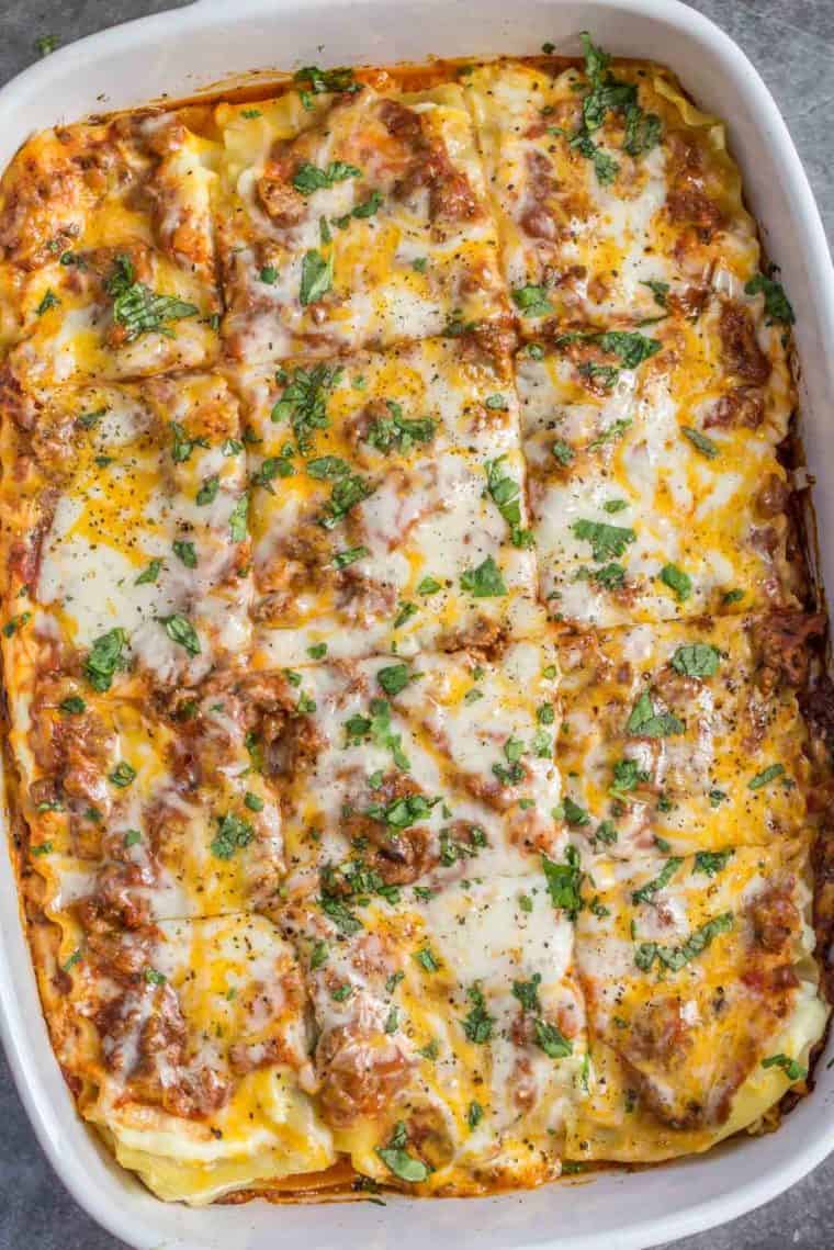 A casserole dish of lasagna sliced into pieces and topped with melted cheese and fresh chopped greens. 