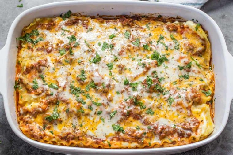 EASY lasagna recipe in a white casserole dish topped with greens.