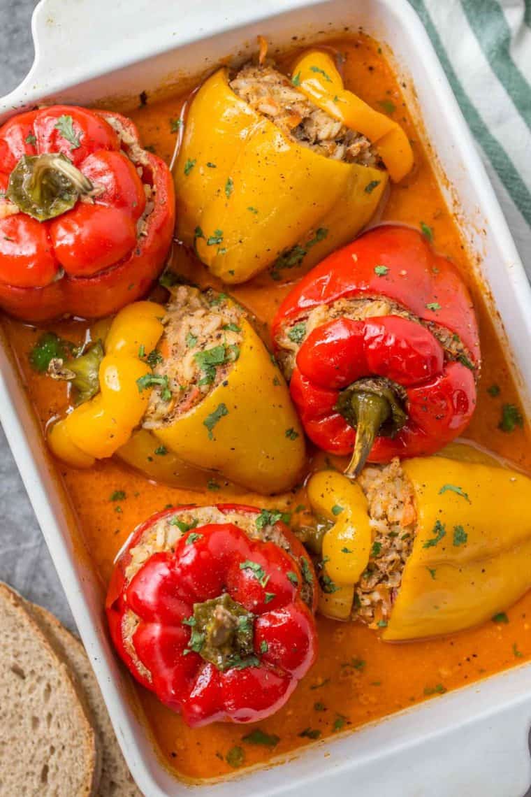 Six stuffed pepper sin a white casserole dish topped with sauce and fresh chopped greens. 