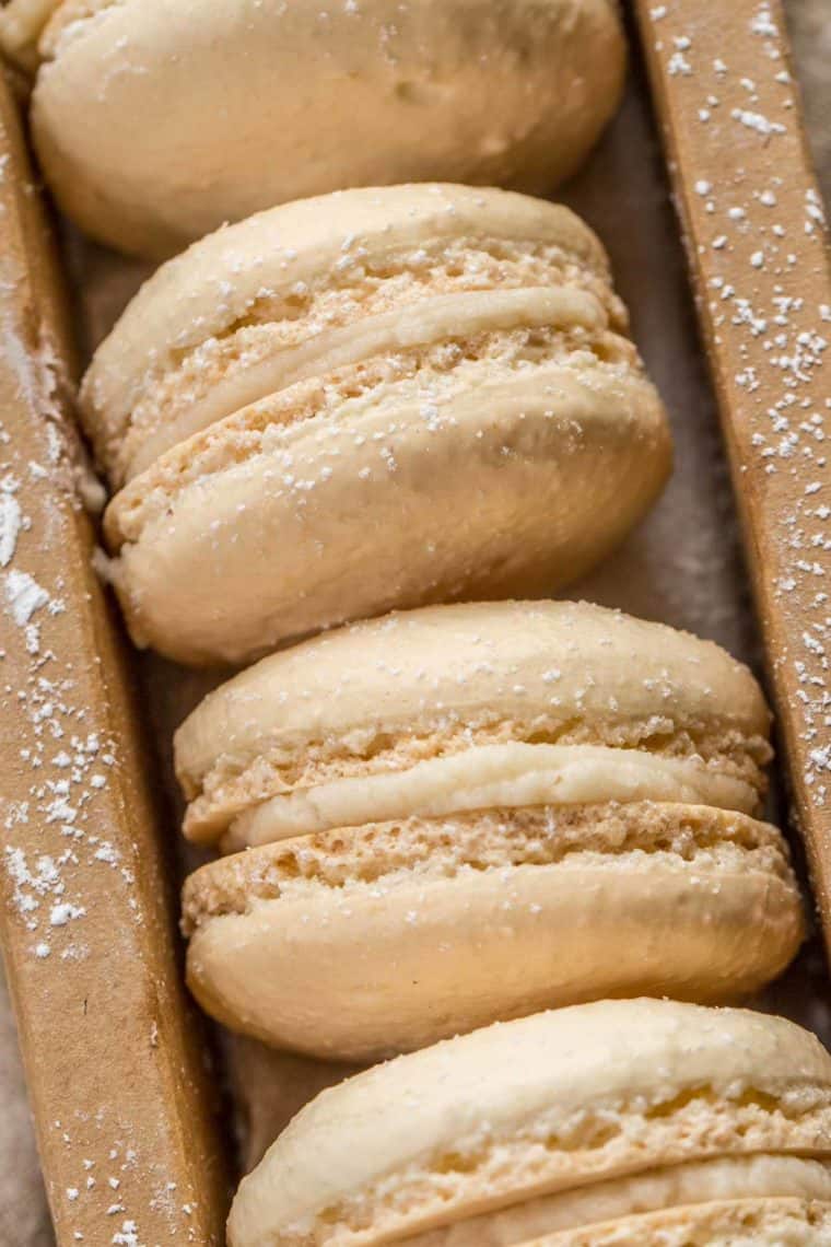 Basic macarons laid out in a brown container topped with powdered sugar.