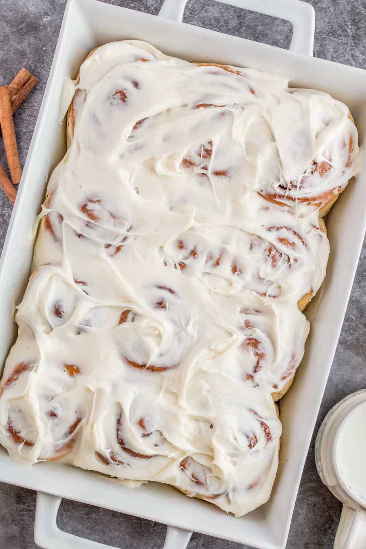 A casserole dish loaded with sweet cinnamon rolls topped with cream cheese frosting.