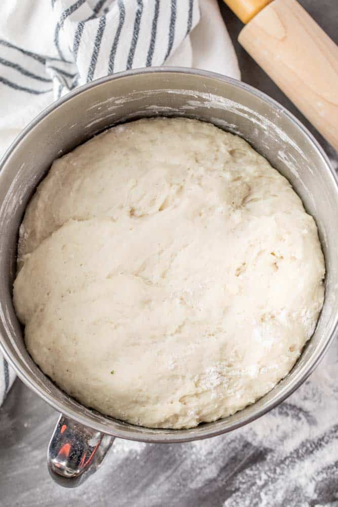 A bowl of risen piroshki dough next to a rag and a roller. 