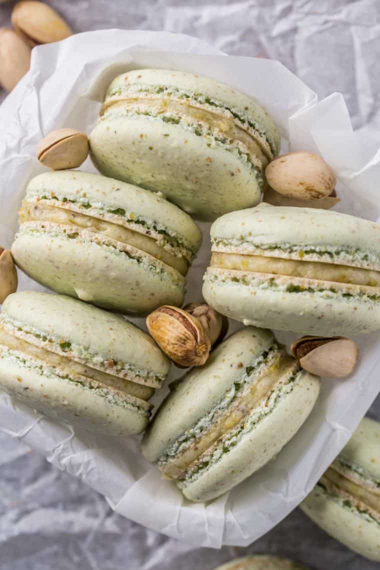 A bowl full of macarons in next to pistachios.