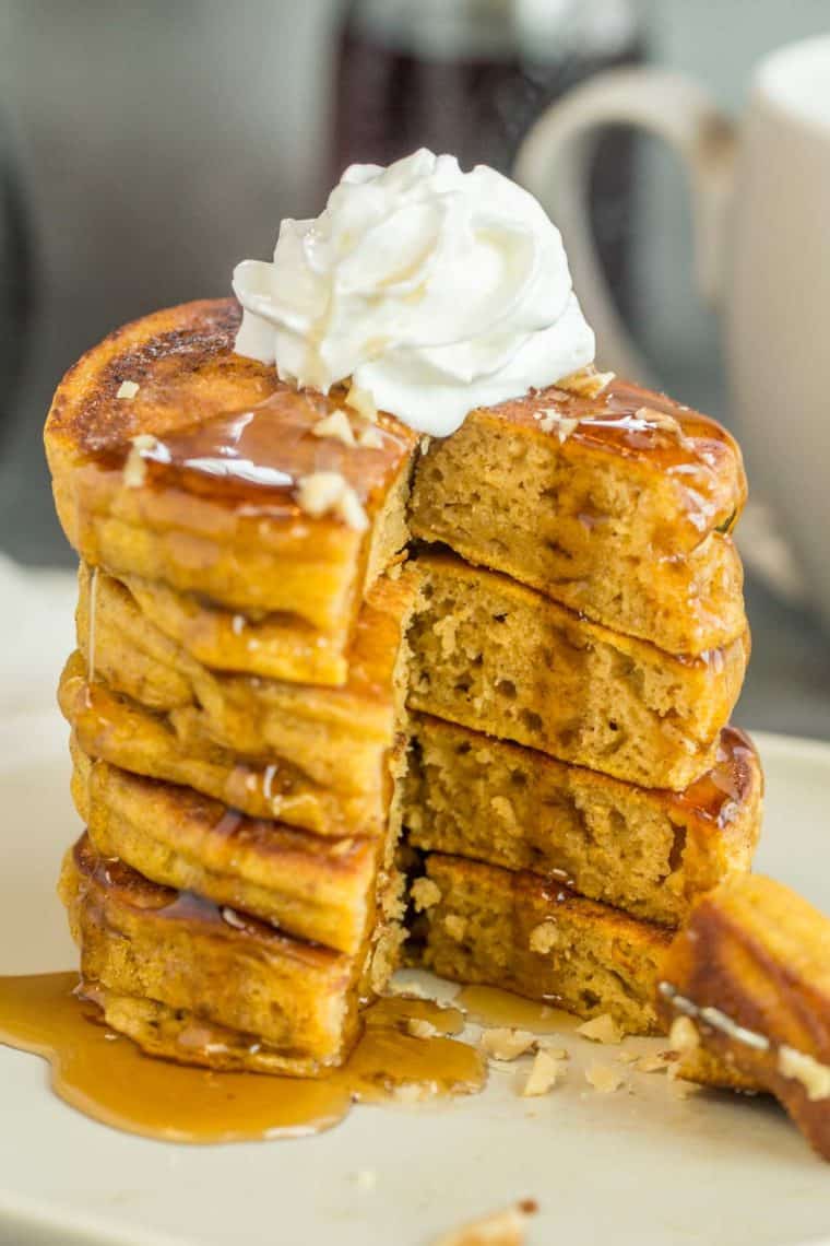 A stack of pumpkin pancakes topped with walnuts, whipped cream, and syrup. 