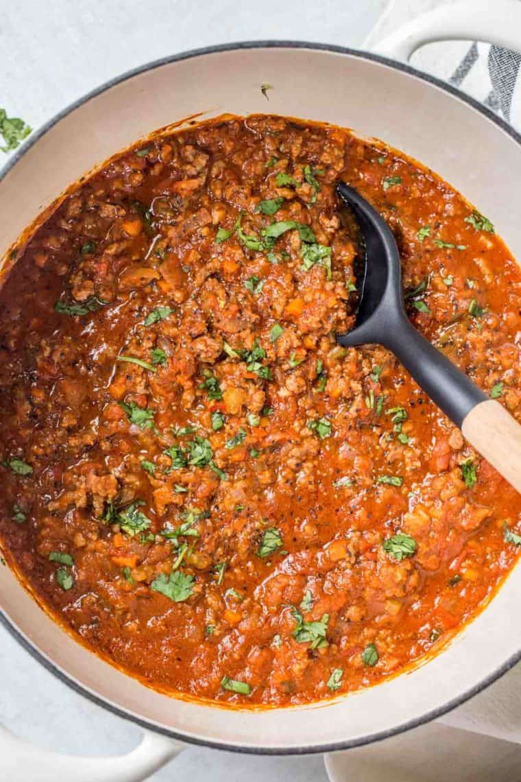 Bolognese sauce in a deep skillet with a spoon in the sauce.