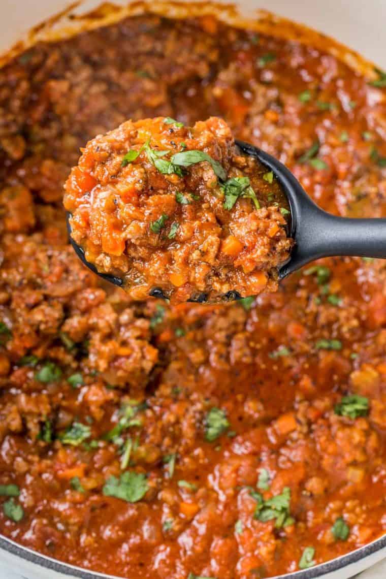 A spoonful of bolognese sauce topped with fresh green in a black spoon.