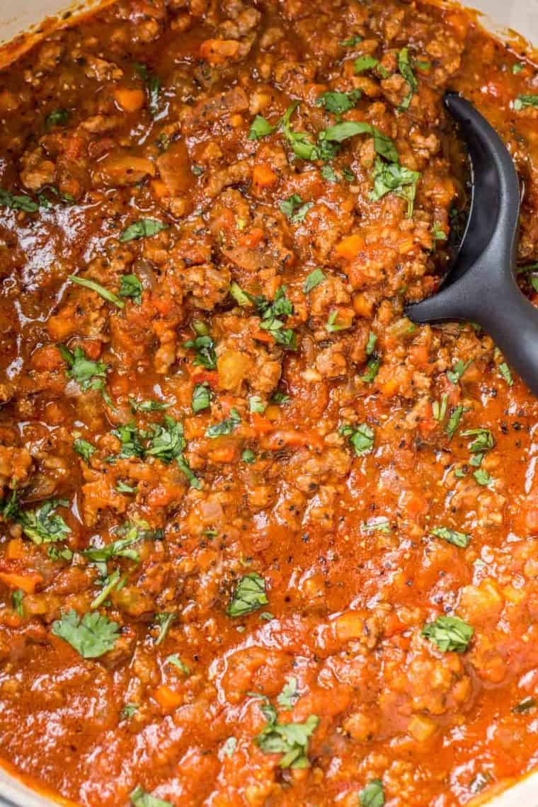 Bolognese sauce topped with chopped greens in a deep skillet. 