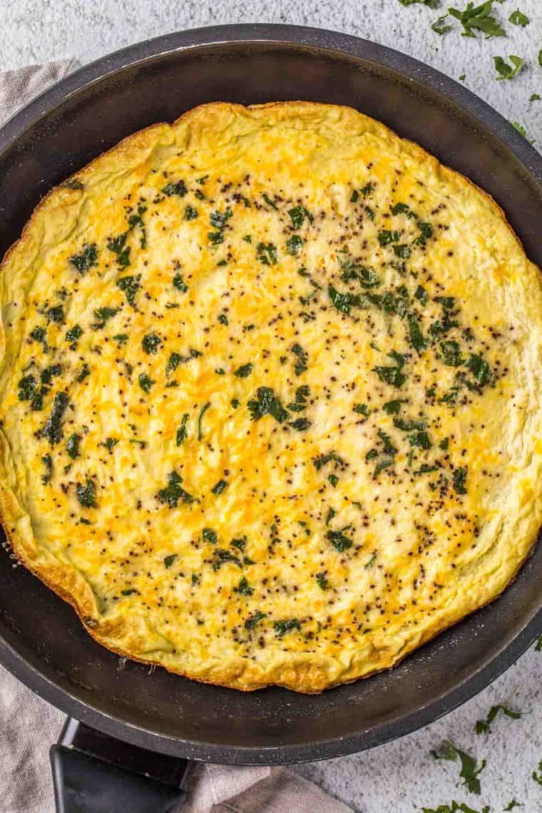 Egg frittata in a black skillet topped with fresh chopped greens. 