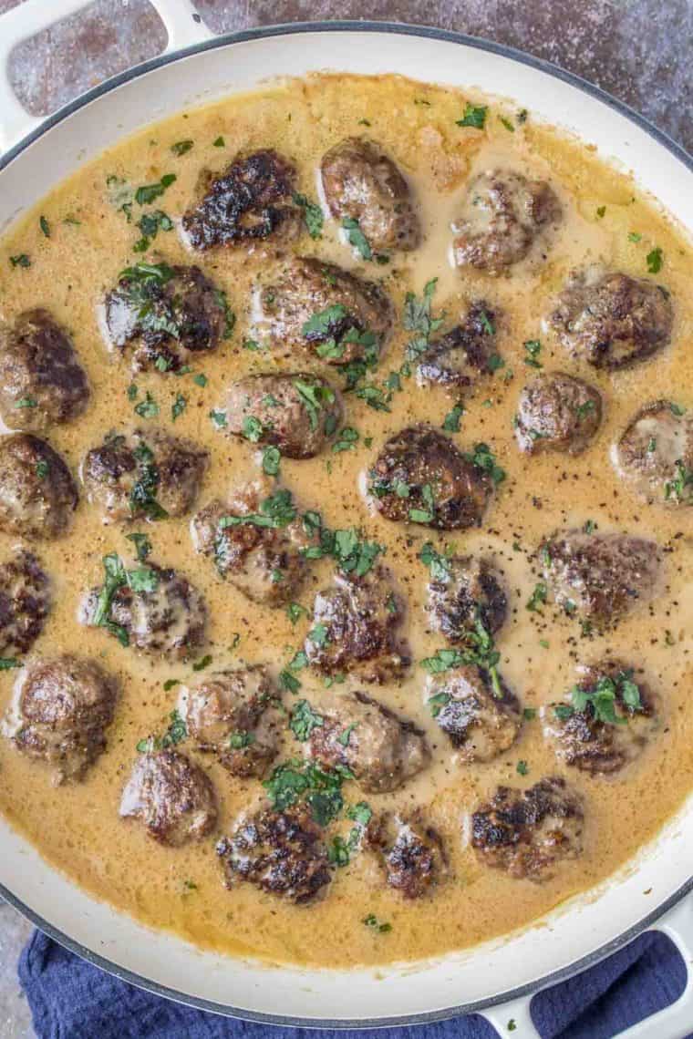 Swedish meatballs in a creamy gravy in white skillet topped with fresh greens.