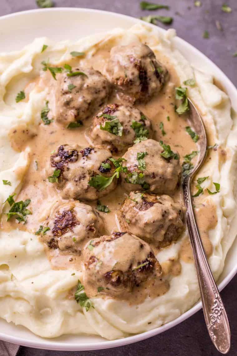 A plate of mashed potatoes topped with meatballs and gravy with a spoon.
