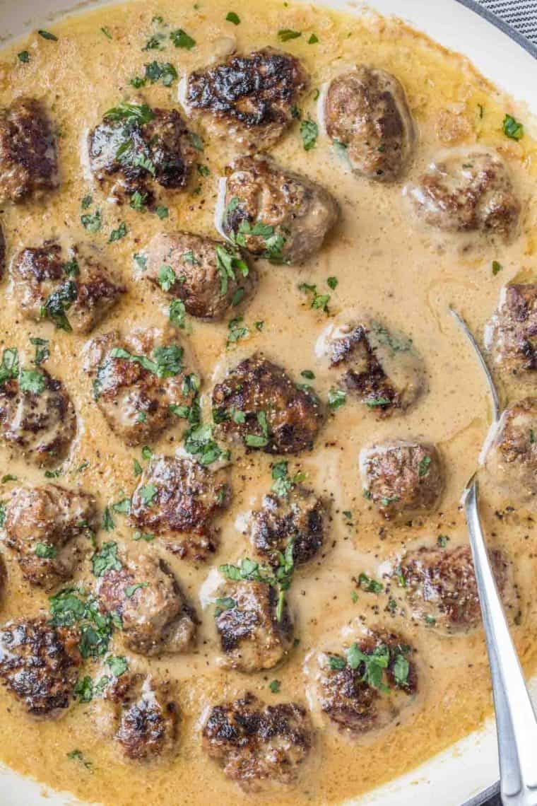 Swedish meatballs in a white skillet topped with chopped greens. 