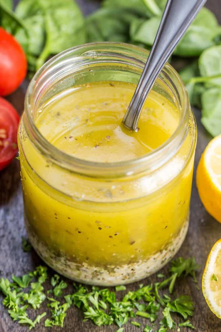 A jar of Italian dressing with a spoon in it next to fresh greens.