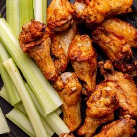Air fried wings on a black plate with celery next to the stack of wings.