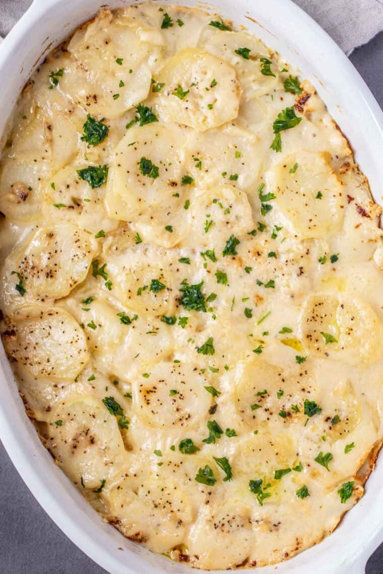 Scalloped potatoes in a white casserole dish topped with fresh chopped greens.