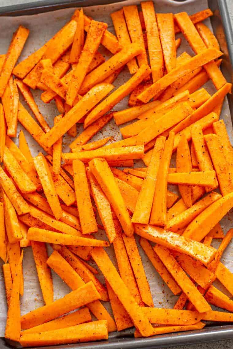 Uncooked sweet potato slices laid out on a baking sheet drizzled in oil and topped with seasoning. 