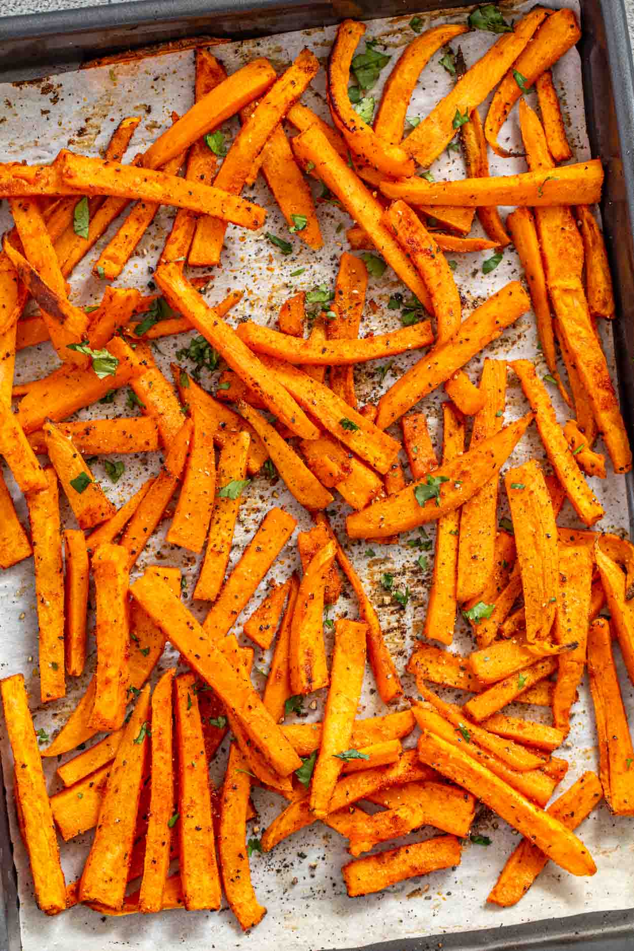 Sweet potato fries on a baking sheet topped with greens.