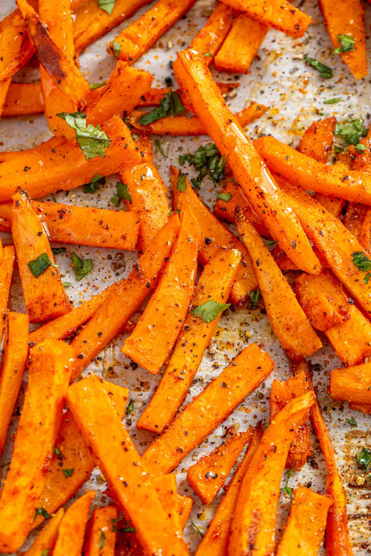 Crispy sweet potato fries laid out on a baking sheet topped with greens and pepper. 