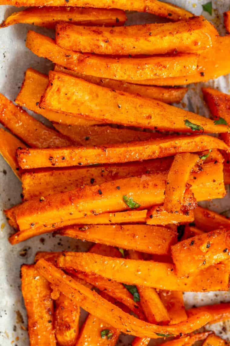 Sweet potato fries stacked in a row and topped with fresh greens and black pepper. 