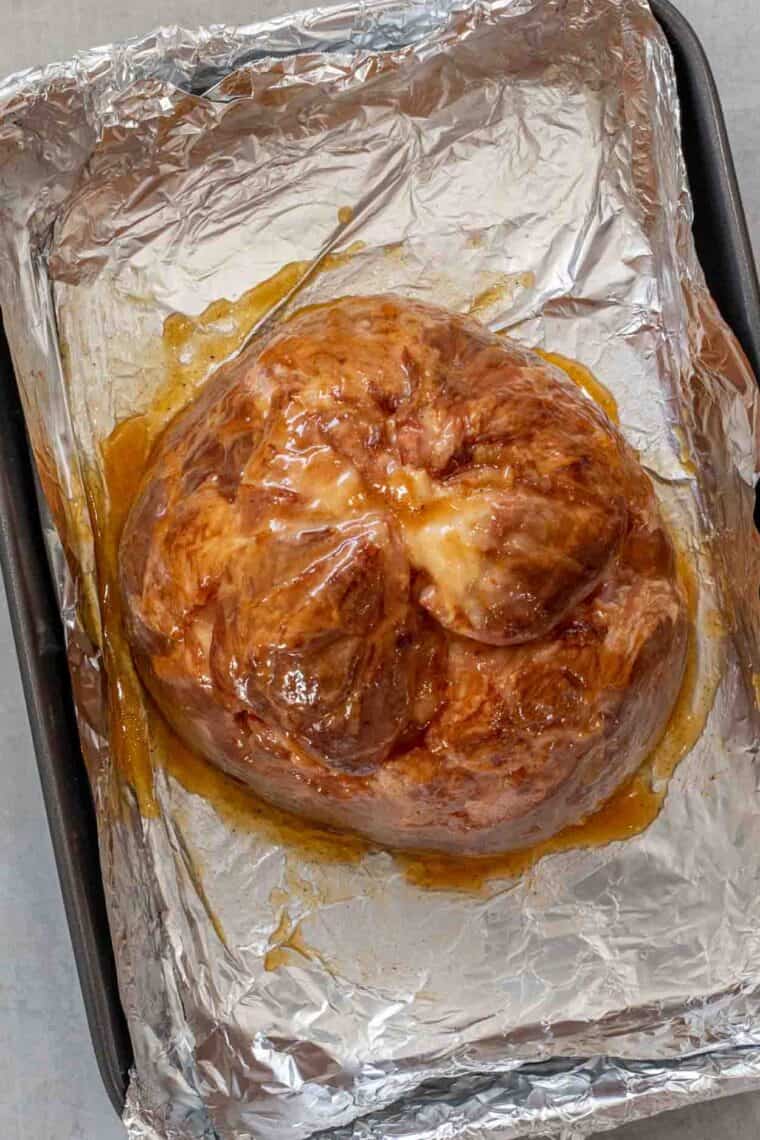 Ham topped with honey glaze in a roasting pan with foil. 