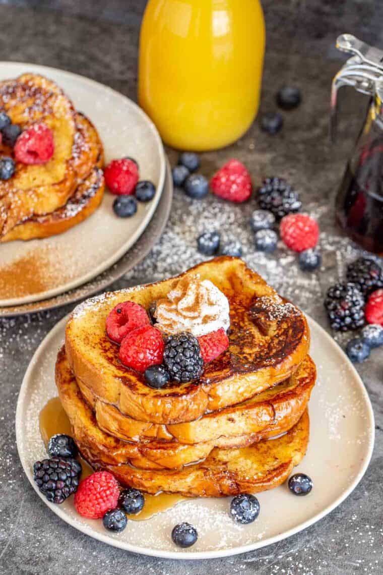 French toast stacked on top of each other topped with whipped cream and fresh berries. 