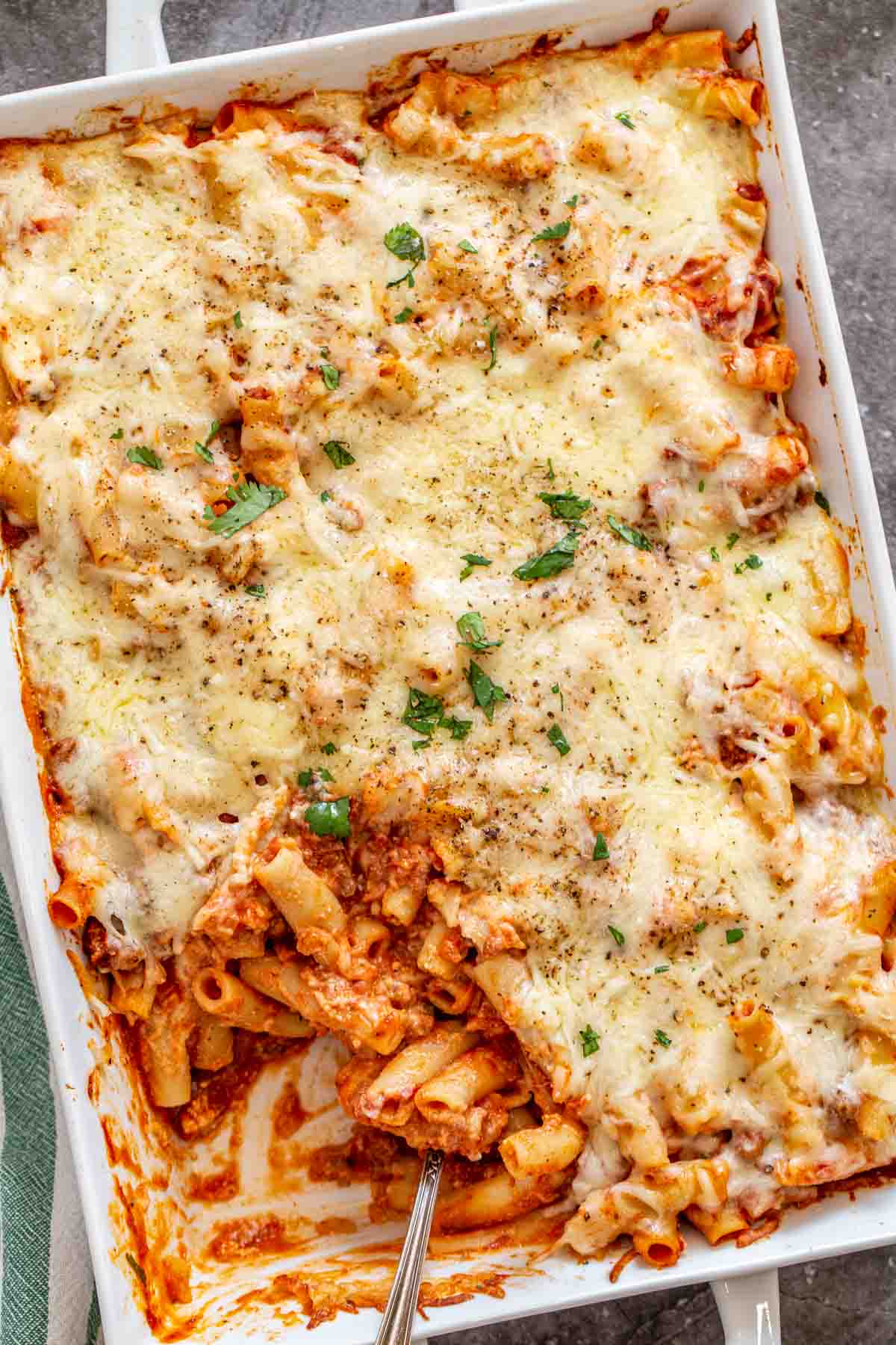 Baked ziti in a white casserole dish topped with fresh chopped greens and black pepper.
