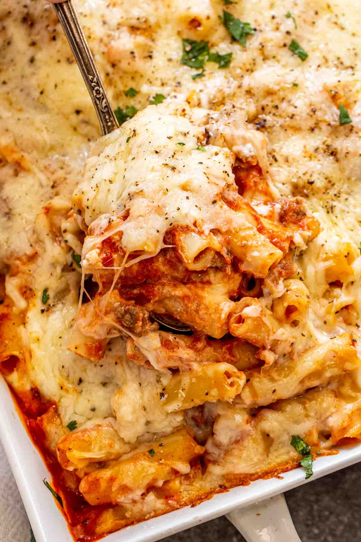 A spoon full of baked ziti with ground beef, cheese and sauce. 