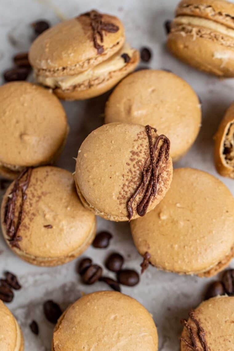Coffee macarons laid out on top of each other next to coffee beans.