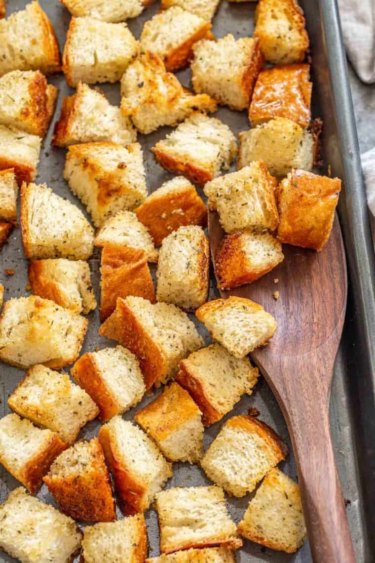 Crunchy baked croutons in a baking sheet with a wooden spoon. 