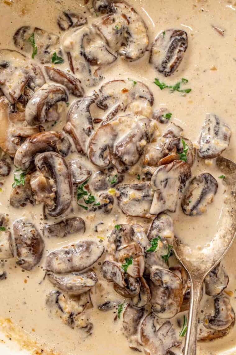 Creamy mushroom sauce topped with fresh greens in a skillet with a metal spoon.