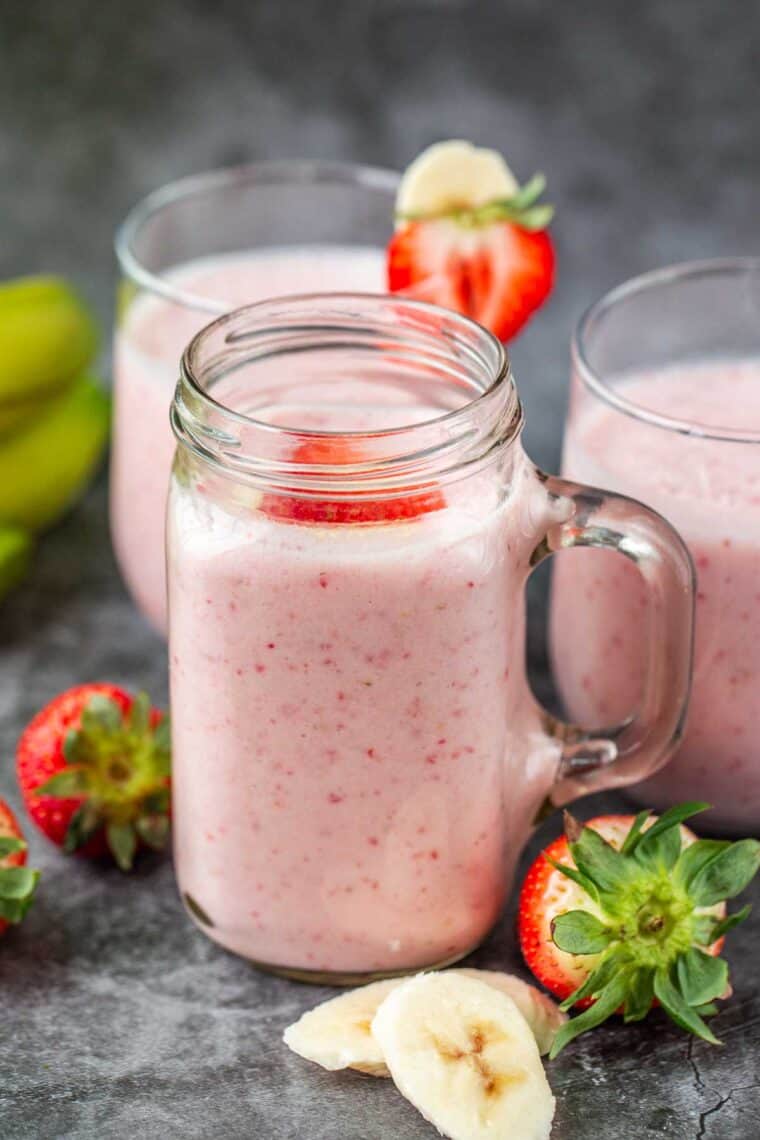 Cups of homemade strawberry banana smoothies next to fresh strawberries and slices bananas. 