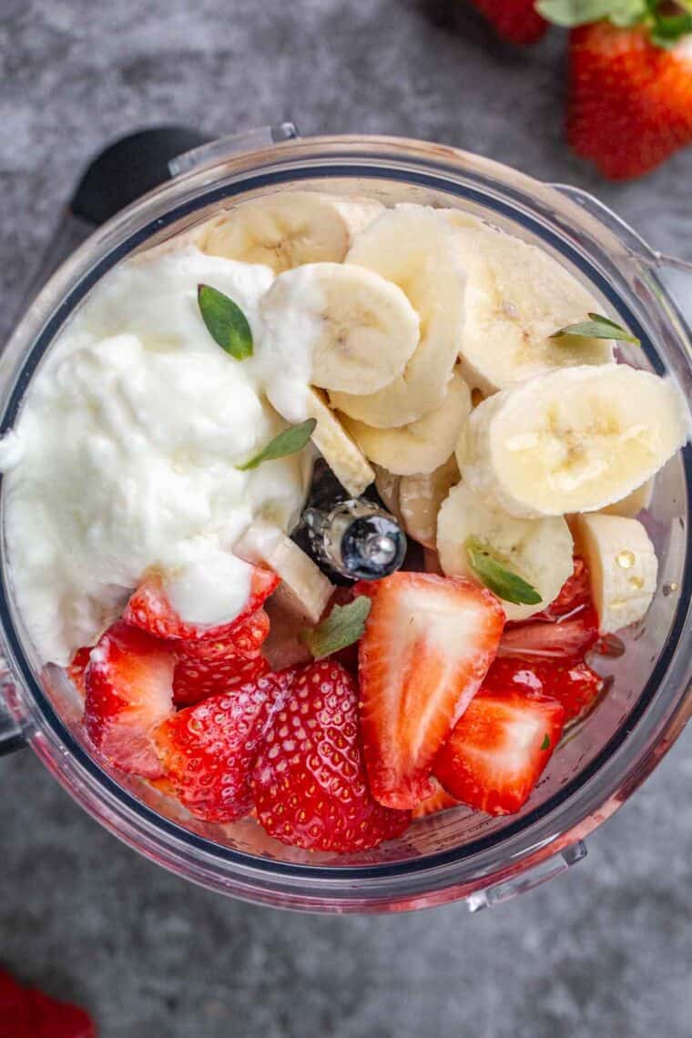 Sliced bananas and strawberries in a blender with honey, milk and yogurt unblended. 