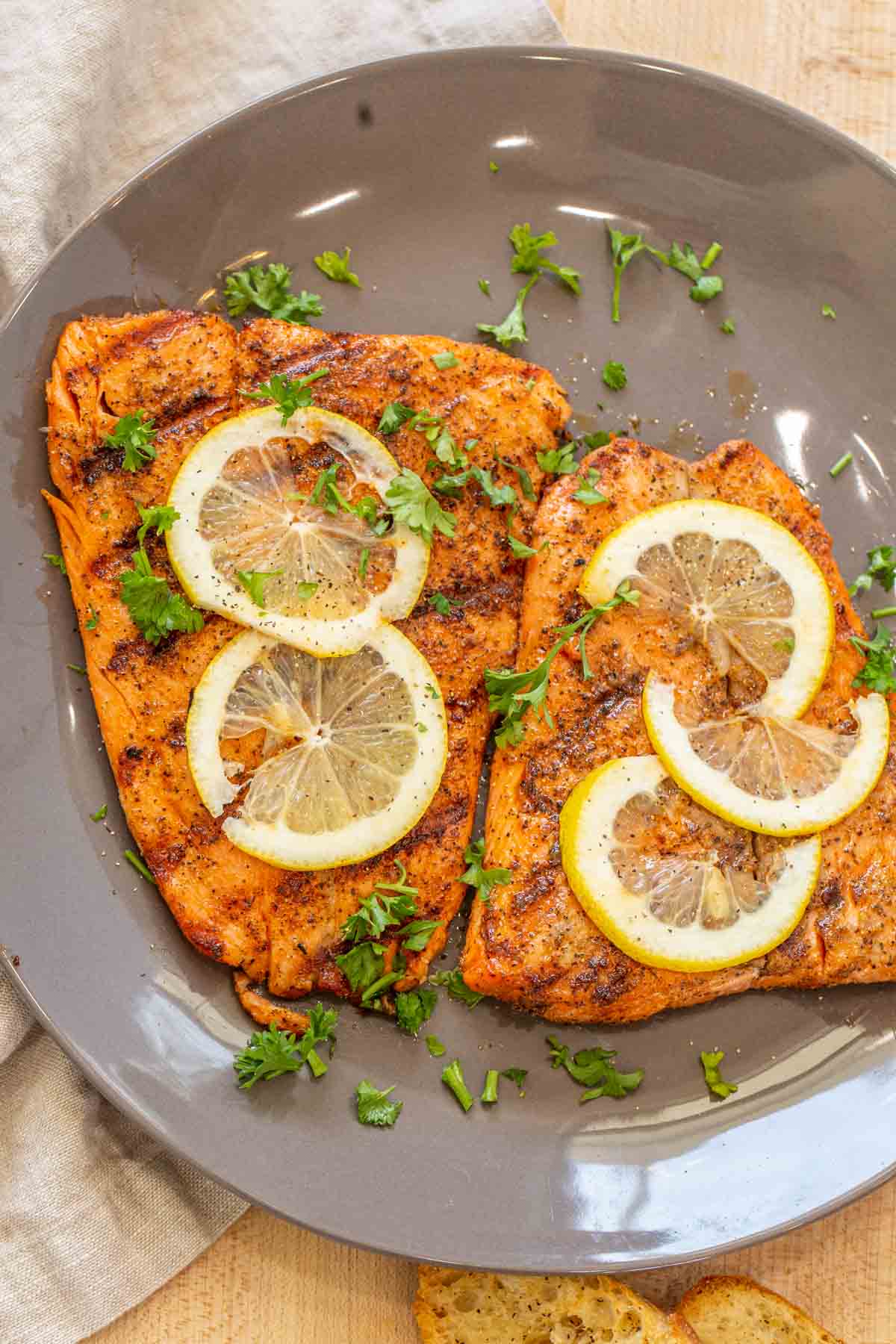 Two grilled salmon fillets on a gray plate topped with lemon slices and fresh chopped greens. 