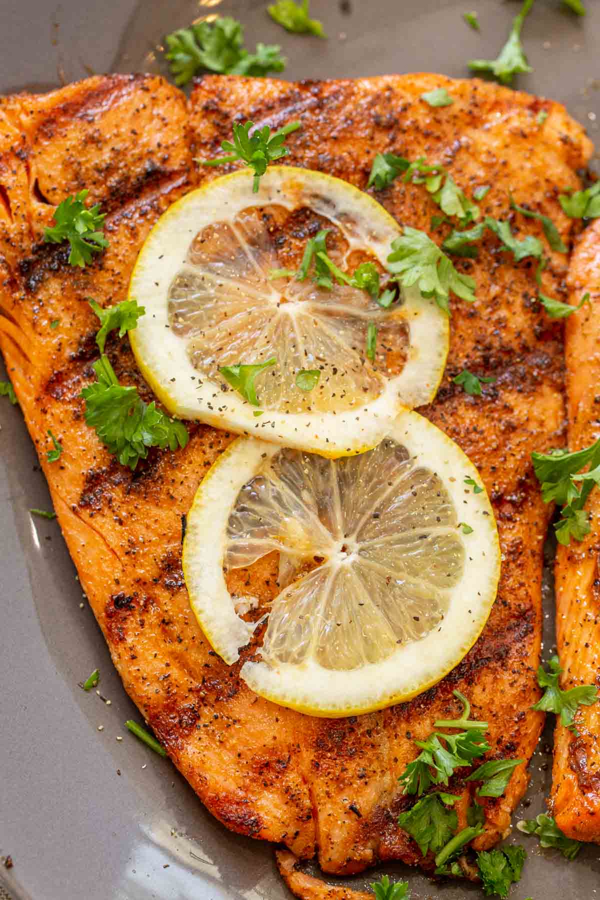 Grilled salmon fillet topped with fresh chopped greens and lemon slices. 