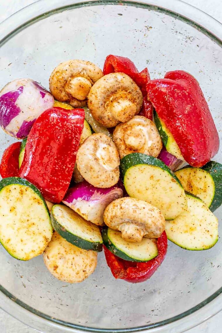 Cut up fresh veggies in a glass bowl marinating in a delicious grilled vegetables marinade. 