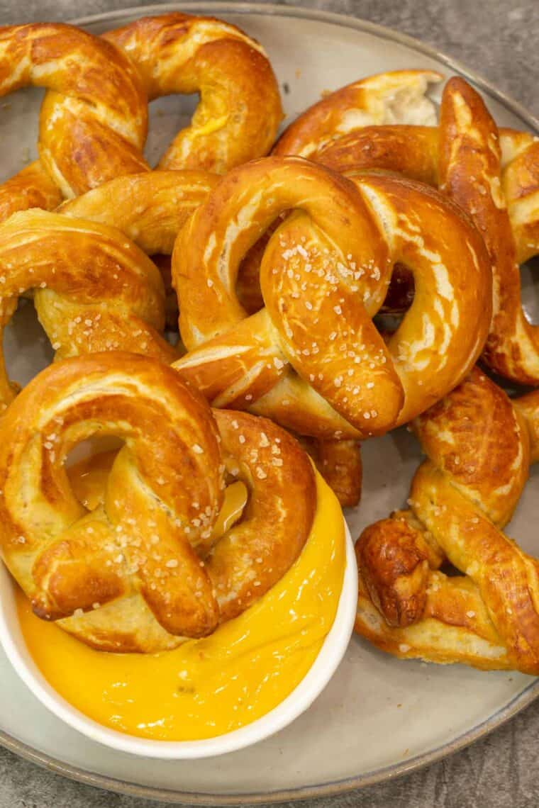 Soft pretzels on a plate next to a white bowl of cheese sauce. 