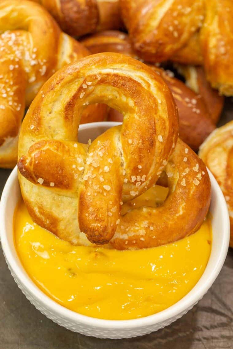 Soft pretzel being dipped into a white bowl full of cheese dip. 