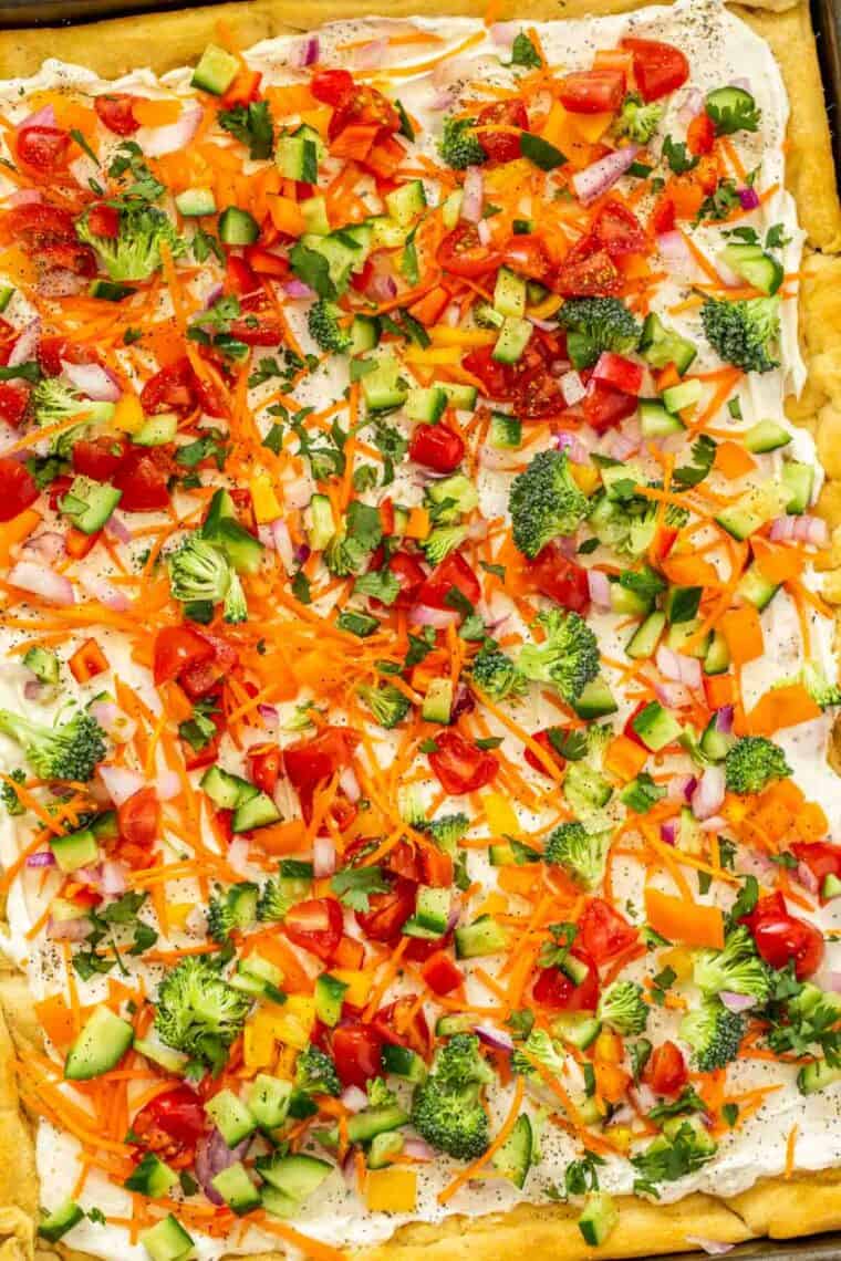 A large baking sheet with cold veggie pizza topped with fresh greens and ground black pepper. 
