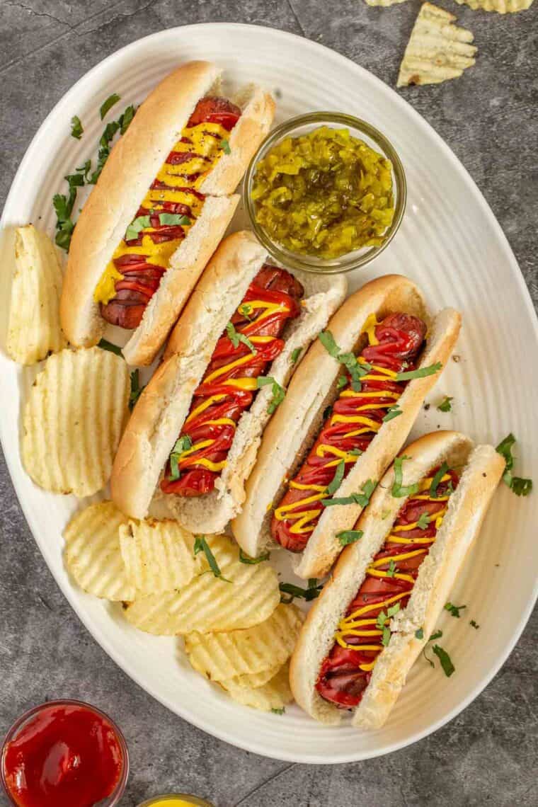 Air fryer hot dogs in a oval white plate topped with ketchup and mustard topped with fresh greens.