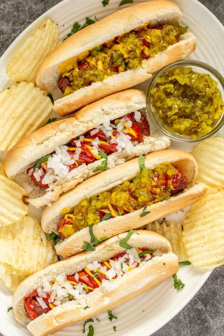 Juicy and crispy air fryer hot dogs topped with the BEST condiments on a white plate with classic chips. 