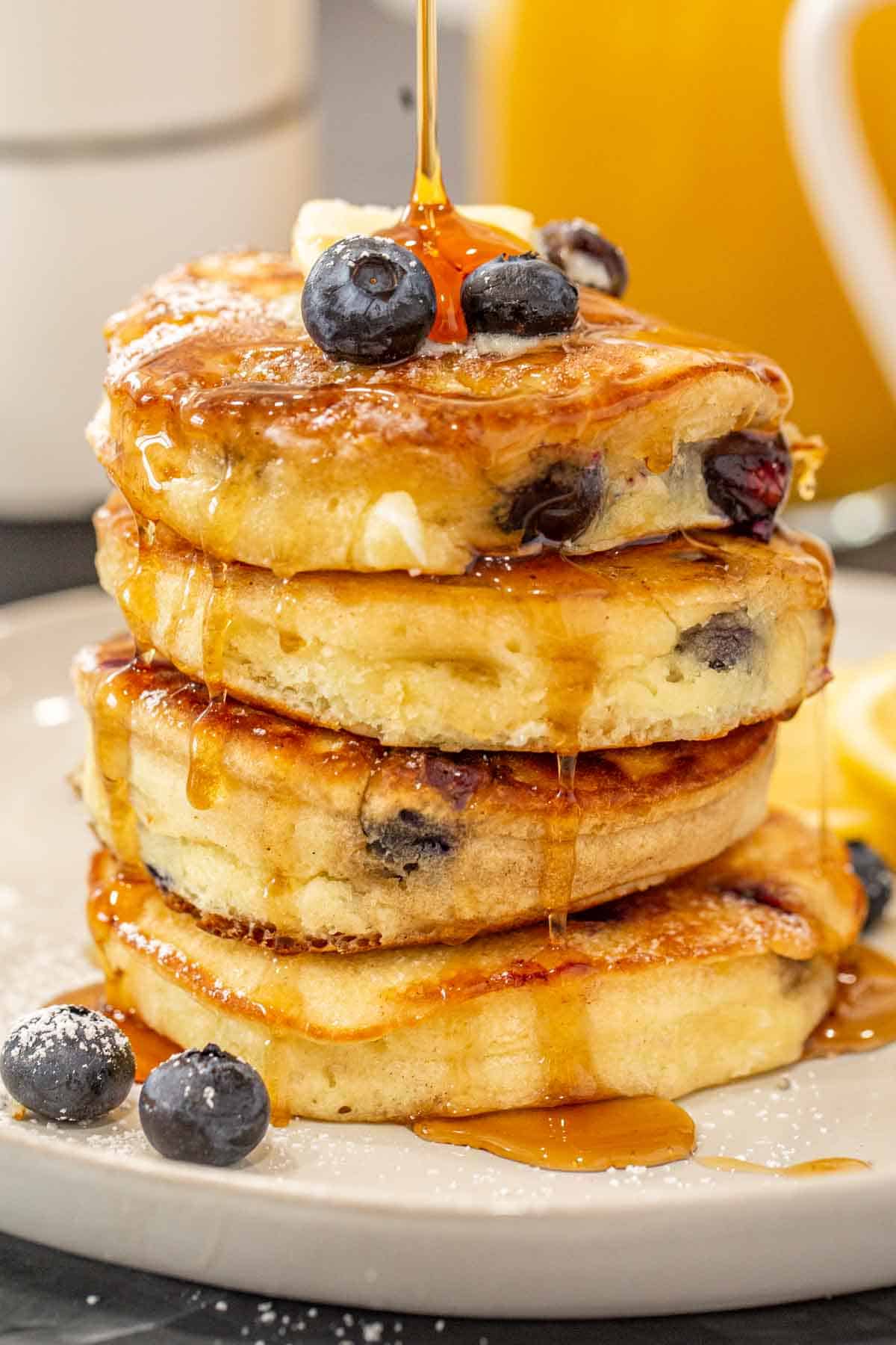 Maple syrup being drizzled on a stack of blueberry pancakes.