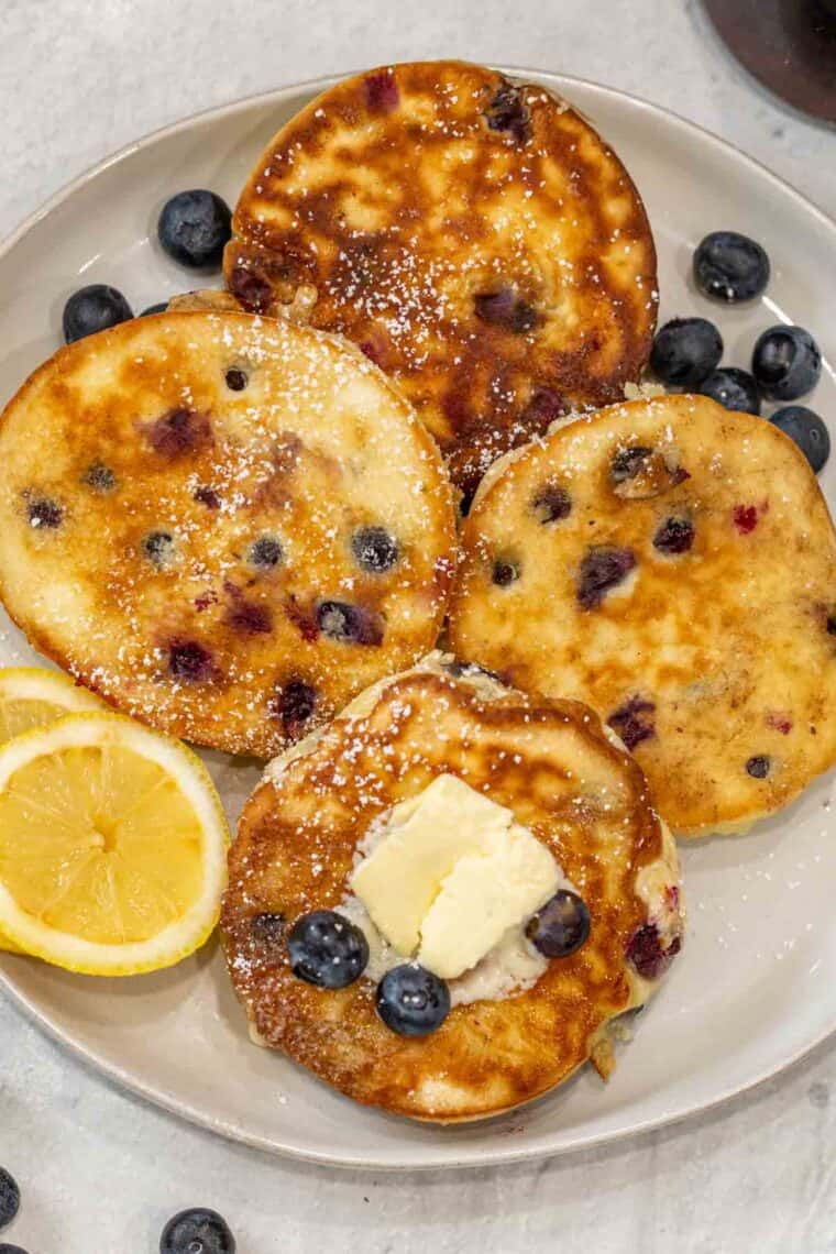 Four pancakes on a plate with blueberries and butter. 