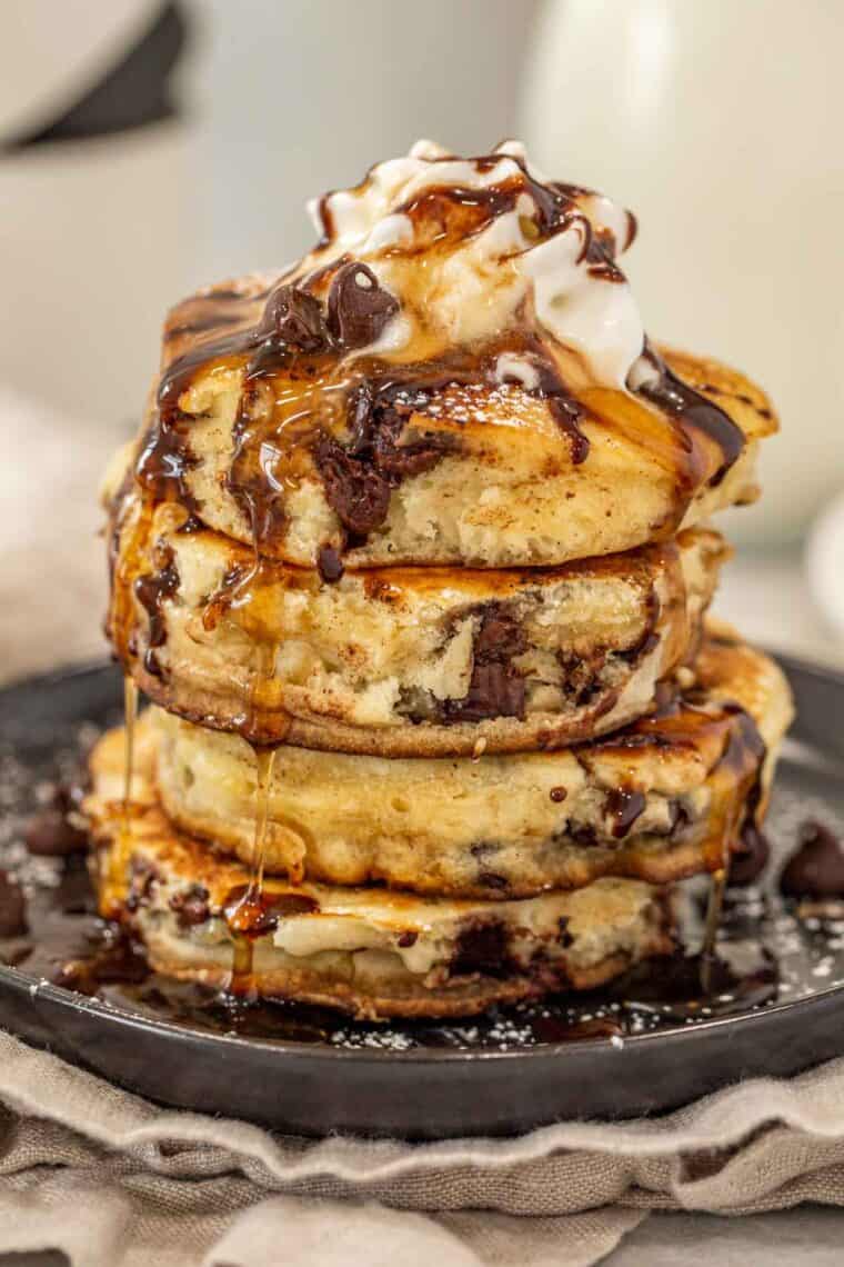 Fluffy and soft pancakes loaded with chocolate chip morsels on a plate topped with whipped cream and chocolate syrup.