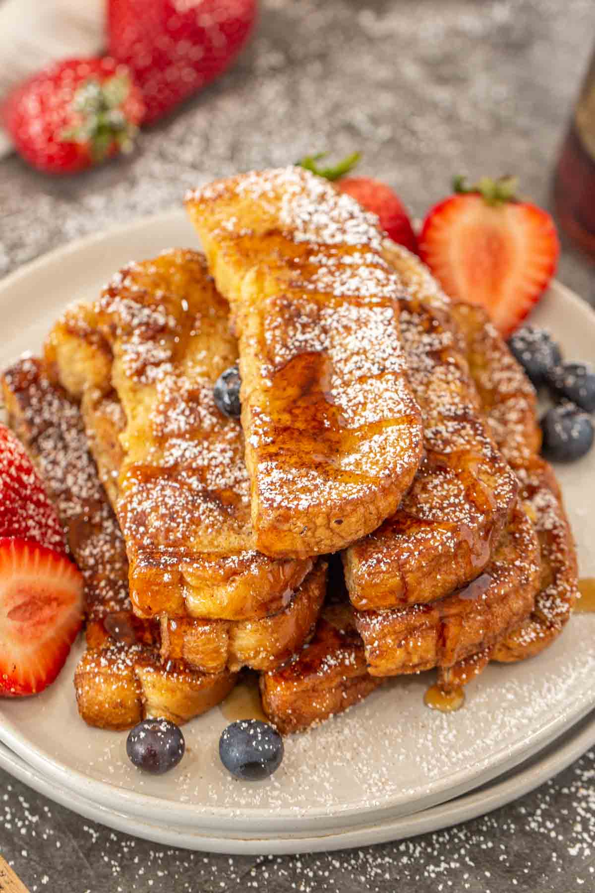 French toast sticks on a plate topped with powdered sugar and maple syrup. 