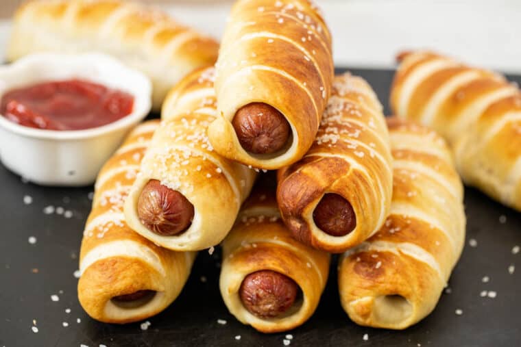 Pretzel dogs stacked on top of each other topped with coarse salt. 